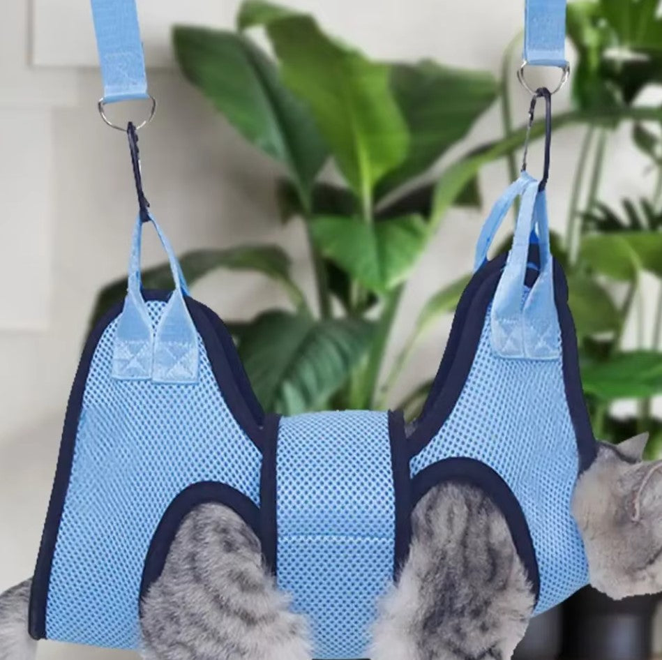 Cat suspended in a grooming hammock while getting its nails trimmed, safe and stress-free grooming tool