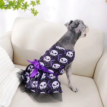 Small dog wearing a Halloween-themed dress with bow and puffy skirt.